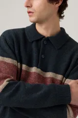 Sweater de punto estilo rugby con cuello polo y cierre frontal de botones. Presenta un diseño de franjas horizontales en tonos azul oscuro, rojo y beige, con puños y ruedo acanalados.