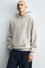 Sudadera tipo hoodie de color blanco hueso, con capucha, manga larga y bolsillo canguro frontal. Presenta un calce relajado y tejido de algodón con interior afelpado.