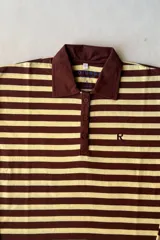 Camiseta polo de manga larga con diseño de rayas horizontales en color marrón y beige, cuello camisero liso en marrón y cierre frontal con botones. Cuenta con una pequeña letra bordada en el pecho.