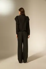 Camisa negra de viscosa con textura arrugada, cuello a la base y cierre frontal con botones. Presenta volados en los hombros y mangas largas.
