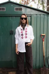 Camisa de algodón color marrón con corte clásico y cuello camisero. Presenta un bordado geométrico en color negro en la parte frontal y mangas largas con puños abotonados.