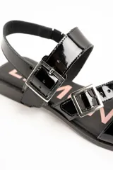Sandalias planas de cuero negro charol con doble tira frontal ajustable mediante hebillas metálicas y tira en el talón.