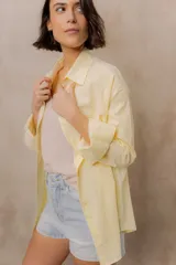 Camisa blanca de calce amplio, confeccionada en tejido liviano con sutiles rayas verticales, cuello clásico, mangas largas con hombros caídos y abotonadura frontal.