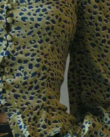 Top de mangas largas abullonadas con escote corazón y cierre frontal de botones. Presenta un diseño ajustado en el torso con un pequeño volado en el ruedo y estampado animal print en tonos verde oliva y negro.