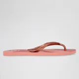 Ojotas de playa Havaianas modelo Elegance Print, color rosa coral con tiras metálicas color oro rosado. La suela presenta un diseño de rayas diagonales en tonos rosados.