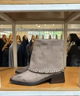 Botas de caña media confeccionadas en cuero gamuzado color gris topo, con diseño versátil 2 en 1 que permite usar la caña extendida o doblada. Presentan un detalle de costura decorativa en contraste en el borde de la caña, puntera ligeramente cuadrada y taco bloque de madera oscuro.