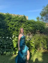 Vestido largo de fiesta color verde esmeralda, con escote halter y argolla en el busto. Presenta cut-outs bajo el busto, espalda descubierta con breteles que se atan en el cuello y falda asimétrica con volados.