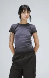 Remera baby tee de manga corta y cuello redondo, confeccionada en tejido ribb de algodón. Presenta un corte ajustado al cuerpo con costuras visibles en los hombros y un acabado de borde crudo en el ruedo.