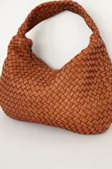 Bolso tipo hobo de cuero marrón oscuro, con diseño trenzado y asa integrada al hombro.