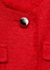 Chaqueta de tweed color rojo con cuello redondo, manga larga y diseño corto. Presenta cuatro bolsillos de parche en la parte frontal, cierre de botones metálicos y terminaciones deshilachadas.