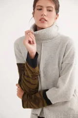 Polera de calce relajado con cuello alto, confeccionada en lana. Presenta un diseño bicolor con cuerpo en gris claro y mangas con estampado jacquard de arabescos en tonos tierra y negro. Incluye detalle de costura central vertical en el frente.