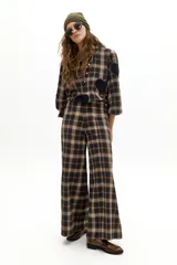Pantalón de pierna ancha con estampado de cuadros en tonos beige, marrón y negro. Presenta tiro medio-alto, cierre frontal oculto y bolsillos laterales de apertura diagonal.