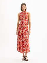 Vestido maxi sin mangas de tejido de punto con estampado floral en tonos rojos, naranjas y blancos, con escote alto tipo polera y frunce frontal en el centro.