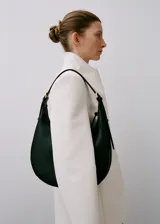 Bolso de hombro tipo hobo con diseño de media luna, confeccionado en material efecto piel. Cuenta con cierre de cremallera, forro interior y asa ajustable con hebillas laterales.