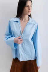 Camisa blanca de algodón, de corte holgado, con cuello clásico, mangas largas con puños anchos y un bolsillo de parche en el lateral.