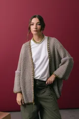 Saco oversize de tejido de punto en color beige, con mangas caídas y detalles de bordado a mano en tonos verde y lila en los bordes y costuras.