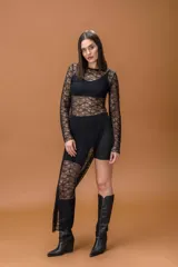 Vestido largo de encaje negro con transparencias, manga larga y cuello redondo. Presenta un diseño con tajo lateral profundo que deja al descubierto la pierna.