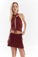 Top halter color bordó con tejido de lurex, escote con tiras cruzadas en el cuello y abertura frontal pronunciada con cordones ajustables.