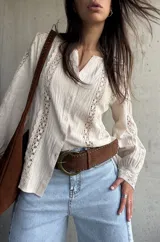 Camisa de manga larga color beige con detalles de encaje y calados verticales en el frente y las mangas, cuello en V y cierre frontal con botones.