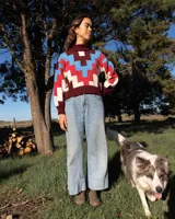 Sweater de cuello alto confeccionado en tejido de punto con diseño geométrico en bloques de colores bordó, rojo, celeste y beige. Presenta puños y ruedo acanalados y un pequeño parche decorativo en el frente.