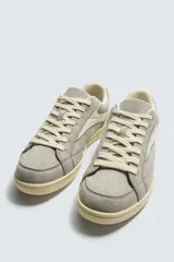 Zapatilla de estilo retro con cordones, confeccionada en una combinación de piezas de gamuza y material sintético. Presenta suela de goma a contraste y diseño de paneles laterales.