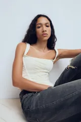 Top estilo corset de color blanco con escote cuadrado y tirantes anchos. Presenta paneles laterales y centrales con tejido drapeado, estructura entallada y cierre posterior con cremallera.