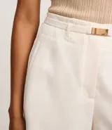 Short de sastre color blanco, tiro alto, corte recto y holgado, con trabillas en la cintura y cinturón elástico con hebilla dorada. Presenta bolsillos falsos en la parte trasera.