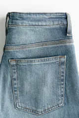 Jean de tiro alto y corte bootcut, confeccionado en denim de algodón levemente elástico con lavado azul medio y efecto desgastado. Presenta diseño clásico de cinco bolsillos, cierre de cremallera y botón metálico.