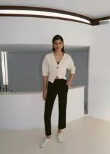 Cardigan de punto fino color crudo, con cuello en V, mangas cortas y cierre frontal con un botón joya en forma de flor.