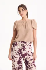 Blusa de manga corta con pliegues en escote redondo, confeccionada en tela crepé de color beige.
