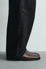 Bota estilo chelsea de cuero color marrón, con paneles elásticos laterales, tirador trasero y horma en punta con suela de tacón bajo.