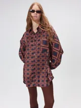 Camisa de seda con estampado geométrico de cuadrados en tonos rojizos y marrones. Presenta cuello camisero, cierre frontal con botones, bolsillo en el pecho y mangas largas con puños abotonados.
