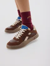 Zapatillas urbanas de cuero con paneles en gamuza negra y detalles en cuero color crema. Presentan suela de goma texturizada en tono marrón y cordones bicolores.