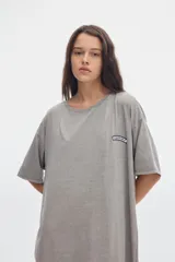 Vestido midi gris con efecto washed, cuello redondo, manga corta, corte recto y holgado, con pequeños tajos laterales en el bajo y un parche bordado en el pecho.