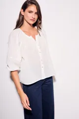 Blusa blanca de algodón peinado, con escote redondo y abertura frontal con botones. Presenta mangas globo de tres cuartos con elástico en el puño y corte holgado.