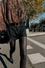 Falda pantalón negra de tiro medio con cierre frontal y hebilla metálica. Presenta bolsillos delanteros y falsos bolsillos de vivo en la espalda.