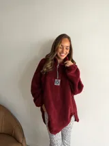 Buzo de corderito color marrón, con cuello alto y cierre frontal parcial. Presenta un diseño holgado con mangas largas y un parche decorativo en el frente.