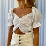 Top blanco de broderie, con escote en V pronunciado, mangas cortas abullonadas y diseño fruncido en el centro del frente.