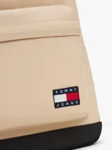 Mochila Tommy Jeans de diseño redondeado en color beige con base negra. Cuenta con compartimento principal con cierre de cremallera, bolsillo frontal con cierre, correas ajustables acolchadas y asa superior. Incluye parche distintivo de la marca en la parte frontal.