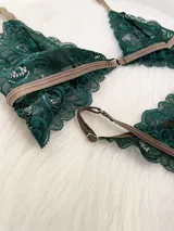 Conjunto de lencería compuesto por un bralette de encaje verde esmeralda con cierre frontal y una tanga a juego con tiras regulables, ambos con detalles de ribetes en color marrón.