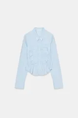 Camisa de algodón con cuello solapa y manga larga. Presenta un diseño con frunces elásticos en el panel frontal y bajo asimétrico. Cierre frontal con botones.