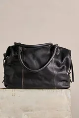 Bolso tote de cuero lavado negro con efecto gastado, interior amplio, bolsillos exteriores con cremallera, dos asas de mano y correa desmontable y regulable.