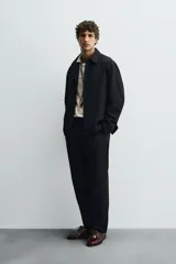 Sobrecamisa negra de corte regular, confeccionada en tejido compacto. Presenta cuello solapa, manga larga con puños abotonados y bolsillos de vivo en la cadera. Cierre frontal con botonadura.