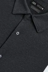 Camisa de corte relajado confeccionada en tejido de algodón con textura. Presenta cuello italiano, manga larga con puños abotonados y cierre frontal mediante botonadura.