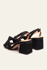 Sandalia de gamuza color beige con taco cuadrado, tira ajustable con hebilla en el tobillo y detalle de nudo en la tira delantera.