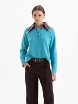 Sweater de punto color azul, con cuello camisero de cuero en contraste con detalles de tachas metálicas y cierre frontal con botones. Presenta mangas largas con puños acanalados y un corte holgado.