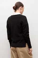 Cardigan negro con escote en V, manga larga y cierre frontal con botones pequeños. Presenta puños acanalados con detalle de botones decorativos.