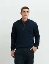Sweater de punto color verde oliva, con cuello alto y medio cierre frontal. Presenta coderas en símil nappa y puños acanalados.