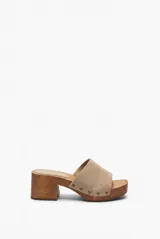 Zueco de taco medio con base de madera, capellada de gamuza beige y detalle de tachas metálicas en los laterales.