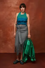 Falda midi color beige de tiro alto y silueta envolvente, con lazo ancho para anudar en la cintura, diseño asimétrico y terminación de flecos largos en el ruedo.